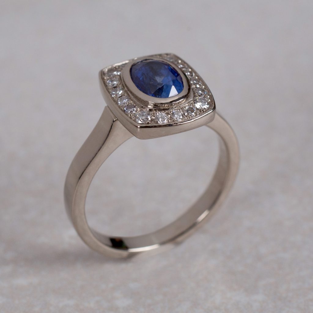 Custom Made 18 Carat White Gold Ring, Set with an Oval Sapphire and 18 Round Brilliant Cut Diamonds.