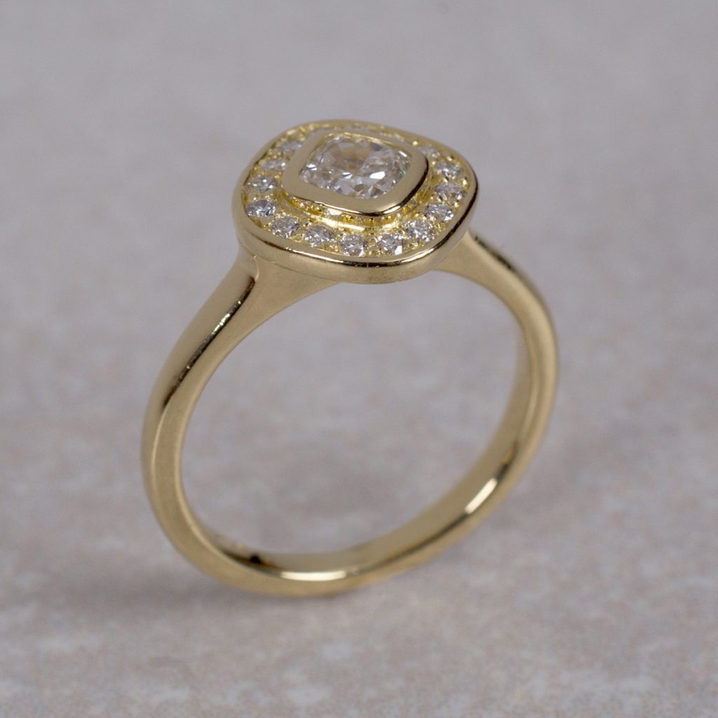 18 Carat Gold Engagement Ring Set with a .54ct Centre Cushion Cut Diamond surrounded by 16 Round Brilliant Cut Diamonds.
